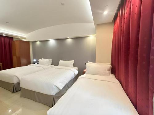 three beds in a hotel room with red curtains at Harbour Bay Hotel in Hong Kong