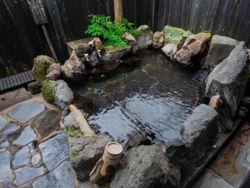 a pond in a garden with rocks and a fence at Yurari Rokumyo in Yufuin