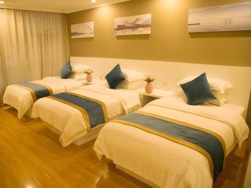 three beds in a hotel room with white sheets and blue pillows at Shell Shanghai Songjiang District Xinqiao Town Xinqiao Hotel in Chunshen