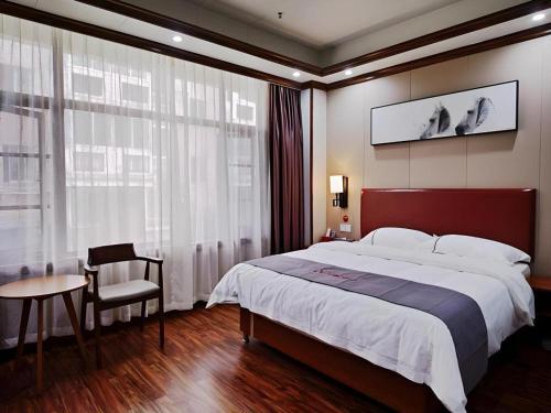 ein Schlafzimmer mit einem großen Bett, einem Tisch und einem Stuhl in der Unterkunft Jun Hotel Guangxi Wuzhou Changzhou District Fengye Garden in Wuzhou