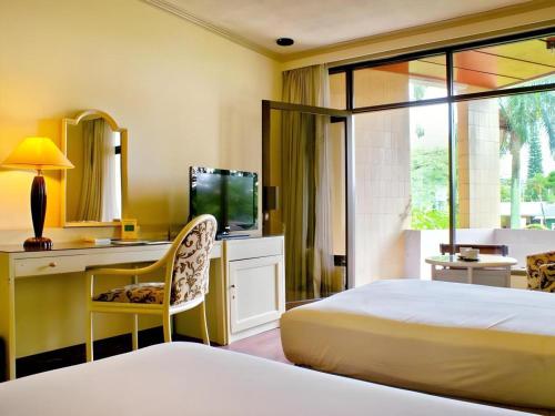 a bedroom with a bed and a desk and a television at Purnama Hotel in Malang