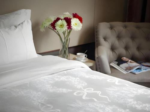 a vase of flowers on a table next to a bed at Hanyong Hotel Shenzhen International Exhibition Center in Shenzhen