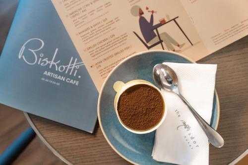 a cup of coffee on a plate next to a book at The Mirador in Mumbai