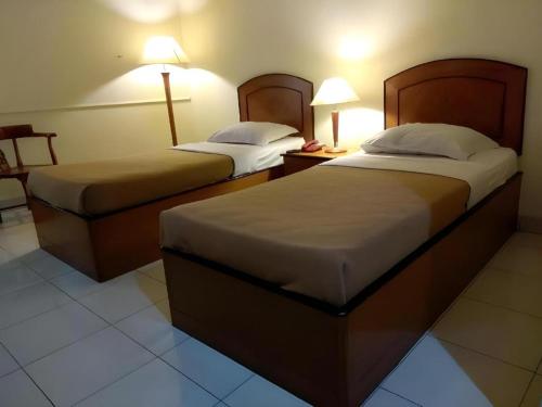 two beds in a hotel room with two lamps at Alexander Hotel Tegal in Tegal