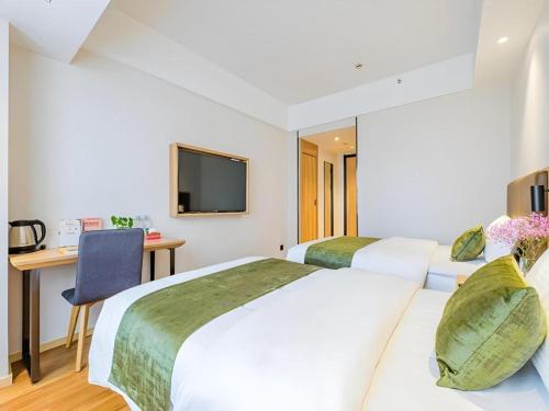 two beds in a hotel room with a desk and a tv at GreenTree Inn Shanghai Jingan Railway Station Xinzha Road Business Hotel in Shanghai