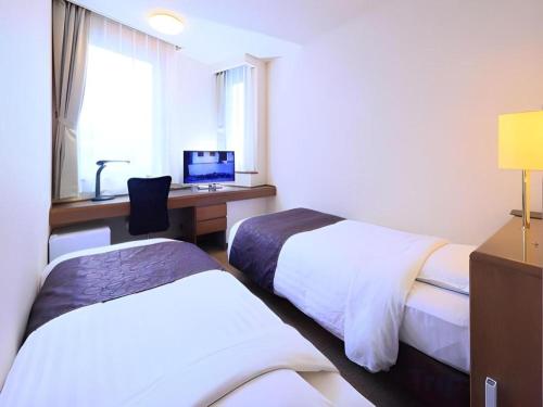 a hotel room with two beds and a desk with a computer at Sunroute Aomori Hotel in Aomori