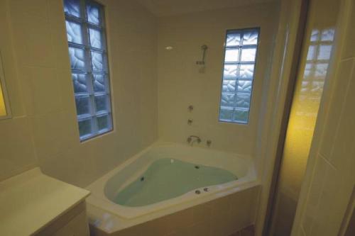 baño blanco con bañera y 2 ventanas en Broke Village Hideaway en Broke