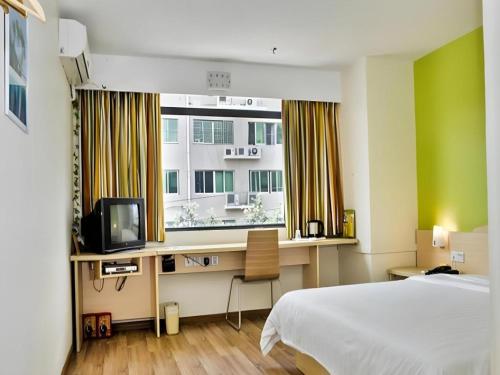 a bedroom with a bed and a desk with a television at 7 Days Inn Guangzhou Zoo Huanghuagang Metro Station in Guangzhou