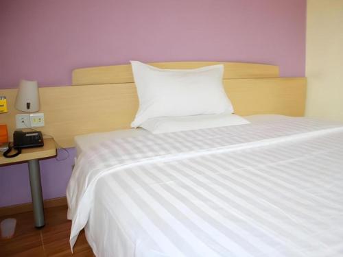 a bedroom with a white bed with a wooden headboard at 7 Days Inn Wuhan Hanyang Wanda Plaza in Wuhan