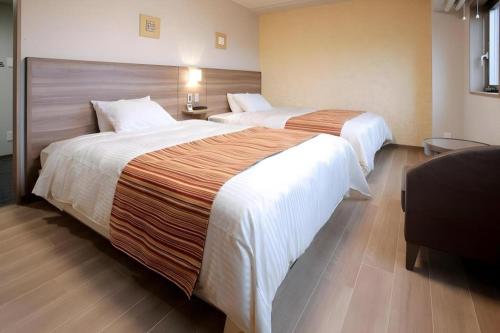 a hotel room with two beds and a chair at Hotel Sunoak Kashiwanoha in Kashiwa