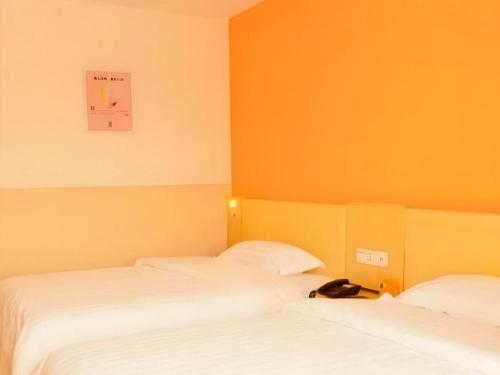 two beds in a room with orange walls at 7 Days Inn Guangrao Bus Station in Dongying