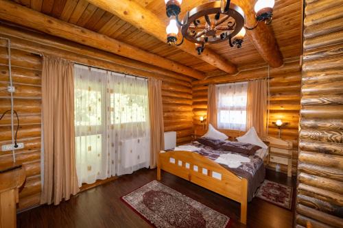 a bedroom in a log cabin with a bed and a chandelier at Pensiunea Moeciu Casa Wiarusti in Moieciu de Sus