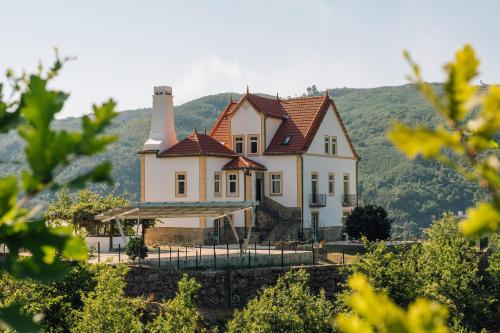 a large house on a hill with mountains in the background at Palacete do Guerreiro Charme Hotel & SPA in Oliveira do Hospital