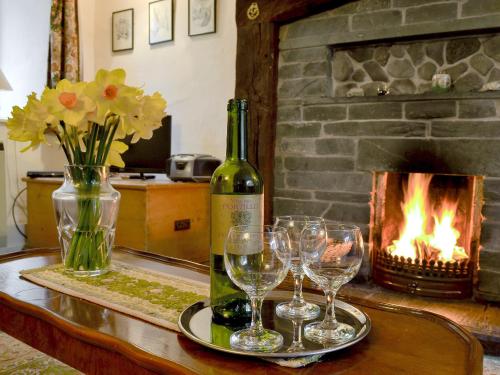 a bottle of wine and wine glasses on a table with a fireplace at Rowlandson Ground Cottage in High Yewdale