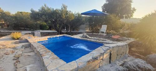 a swimming pool in a stone wall with an umbrella at Apartman Olive grove in Rogoznica