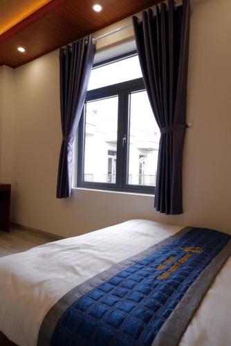 a bedroom with a large window with blue curtains at Diamond Luxury Hotel & Café Măng Đen in Kon Plong