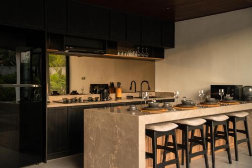 a kitchen with black cabinets and a counter with bar stools at The Placo Villa Uluwatu in Denpasar