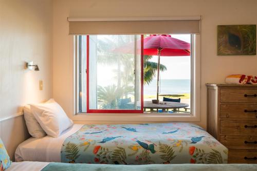 a bedroom with a bed and a window with a view of the beach at Driftwood Lodge Beachfront, Cable Bay Stays, Cable Bay, Northland in Coopers Beach