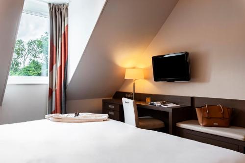 a hotel room with a bed and a desk and a tv at Mercure Bayeux Omaha Beach in Port-en-Bessin-Huppain