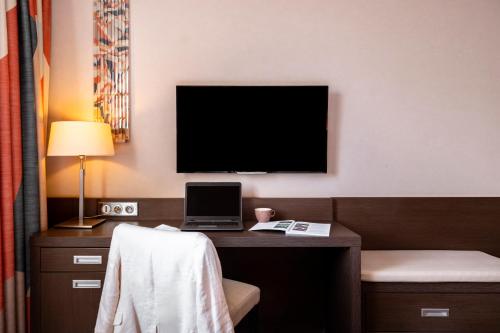 a hotel room with a desk with a laptop and a television at Mercure Bayeux Omaha Beach in Port-en-Bessin-Huppain