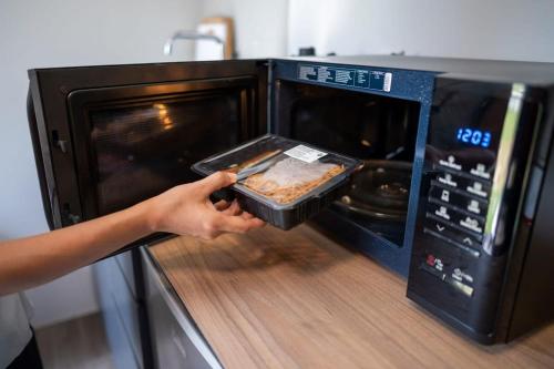 a person holding a pan of food in a microwave at Tiny Away Escape at Lazarus - 1960 in Singapore