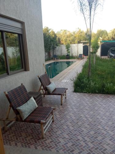 two chairs sitting on a patio next to a swimming pool at charmante villa à découvrir in Aghmat
