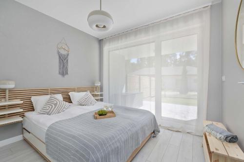 a white bedroom with a bed and a large window at Urokliwy Apartament z Ogródkiem 150 m od Plaży Parking Międzywodzie by Noclegi Renters in Międzywodzie
