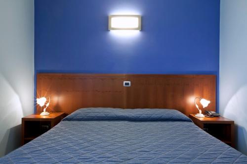 a bedroom with a blue wall and a bed with two lamps at Hotel San Martino in Cassibile