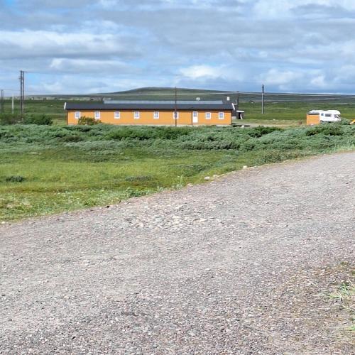 a building in a field next to a gravel road at Svartbakken Rooms in Vardø