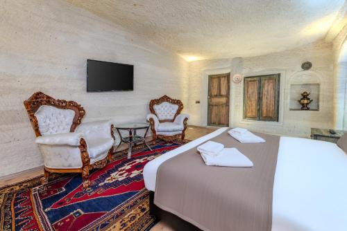 a bedroom with a bed and two chairs and a tv at Kayatas Cave Suites in Goreme