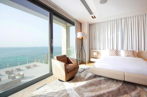 a bedroom with a bed and a chair and a large window at Luxurious Overwater Villa Escape on Nurai Island in Abu Dhabi