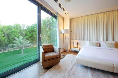 a bedroom with a bed and a chair and a large window at Luxurious Overwater Villa Escape on Nurai Island in Abu Dhabi