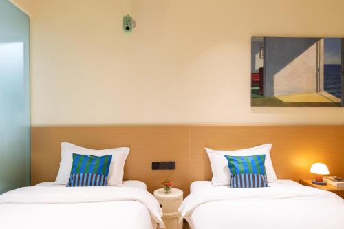two beds in a hotel room with a painting at Xiamen Evening Breeze Hotel in Xiamen