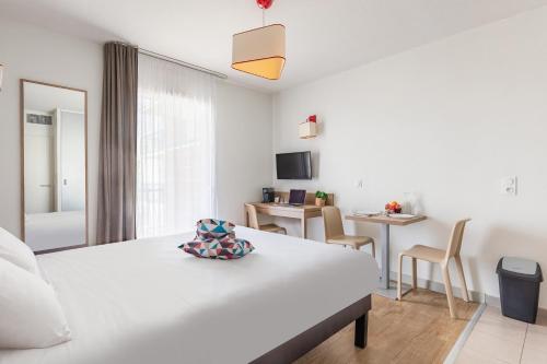 a white bedroom with a bed and a table and chairs at Appart'City Confort Perpignan Centre Gare in Perpignan