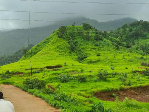a green grassy hill with a person standing on a dirt road at Shafi Villa in Neral