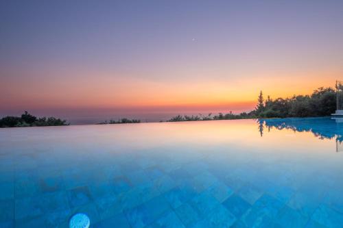 a swimming pool with a sunset in the background at NEW LUXURY STONE Villa AMENTE in Fiskardho