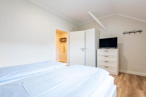 een witte slaapkamer met een bed en een televisie bij Steger-Hüs Wohnung 37 in Rantum