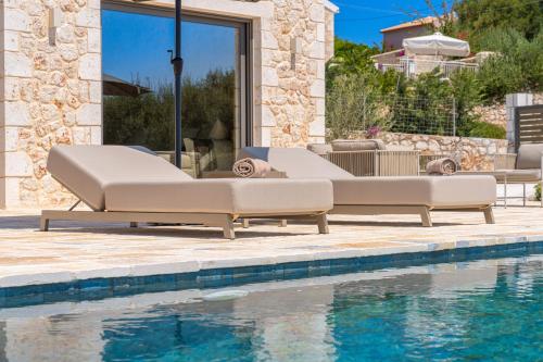 a pair of white lounge chairs next to a pool at NEW LUXURY STONE Villa AMENTE in Fiskardho