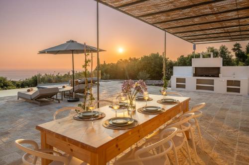 a wooden table and chairs on a patio with the sunset at NEW LUXURY STONE Villa AMENTE in Fiskardho