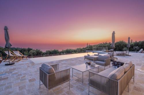 a patio with couches and tables and a sunset at NEW LUXURY STONE Villa AMENTE in Fiskardho
