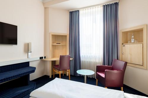 a hotel room with a bed and two chairs and a desk at Rugs Hotel Augsburg City in Augsburg