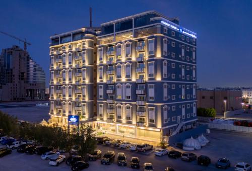 a tall building with cars parked in a parking lot at Sumou Hotel Al Khobar in Al Khobar