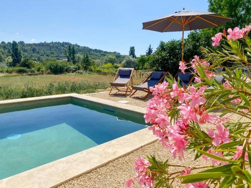 a pool with two chairs and an umbrella and pink flowers at Radegonde - Maison de charme avec piscine in Rustrel