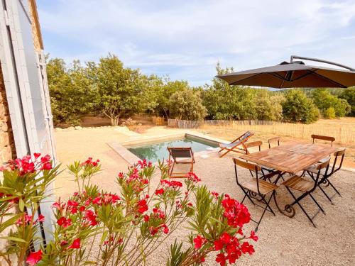 a patio with a table and an umbrella and flowers at Radegonde - Maison de charme avec piscine in Rustrel