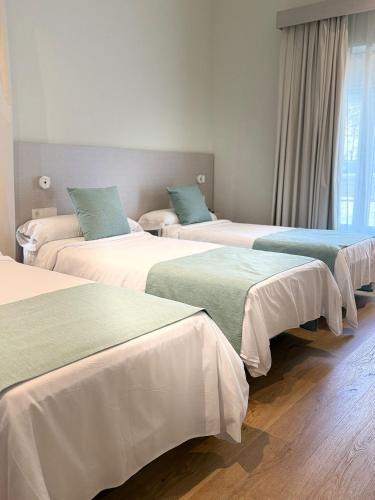 a room with three beds with white and green sheets at Hotel Bon Repòs l'Ametlla de Mar in L'Ametlla de Mar