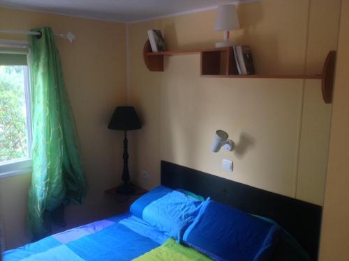 a bedroom with a bed with blue sheets and a window at Charmant mobil home au Cap Ferret, idéalement situé dans un camping 4 étoiles Sibulu les Embruns à Claouey in Lège-Cap-Ferret