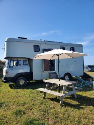 a picnic table with an umbrella next to a camper at Monroe Horsebox Glamping in Porthleven