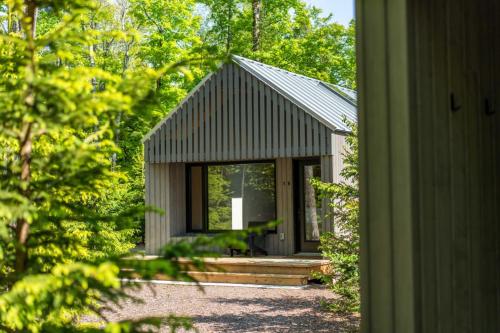 a small cabin with a porch in the woods at Forest Edge Escape at Dimensions - Cabin Sixteen in Algonquin Highlands