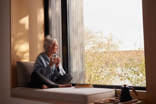 a woman sitting on a window sill drinking a drink at Tranquil Waters at Dimensions - Cabin Two in Algonquin Highlands
