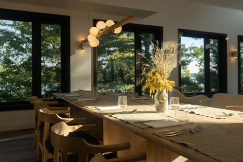 a dining room with a long table with chairs and windows at Nourish and Reset at Dimensions - Cabin Ten in Algonquin Highlands